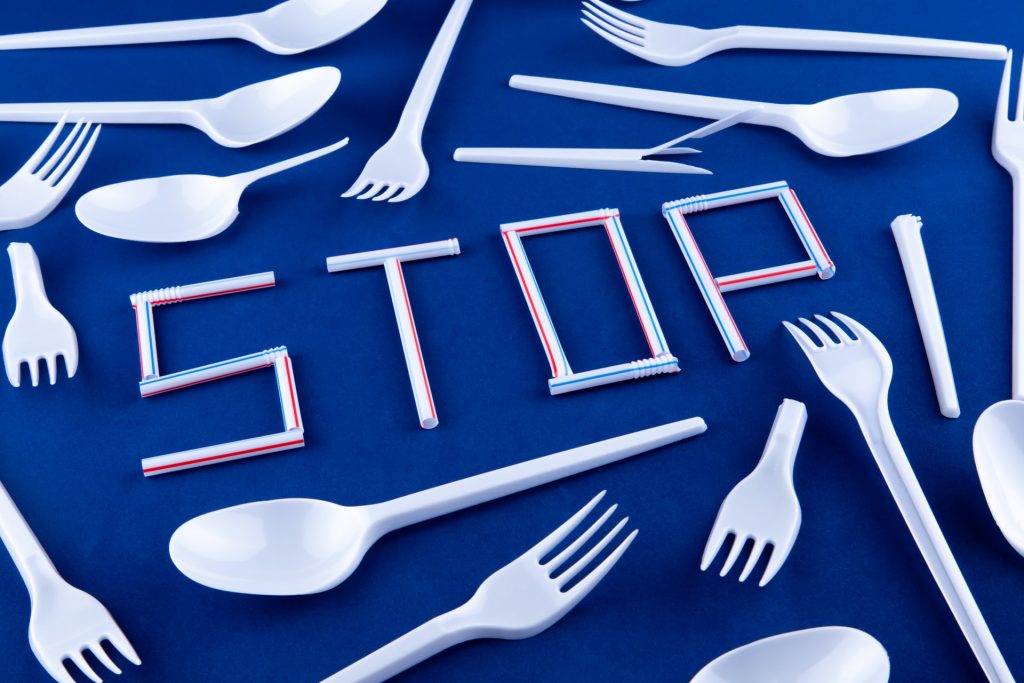 The word stop is written on a blue surface with plastic whistles. Disposable spoons and forks in the background.