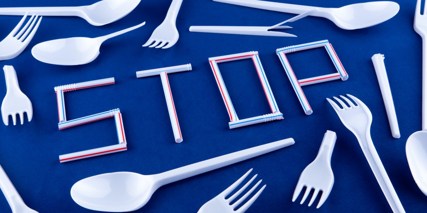 The word stop is written on a blue surface with plastic whistles. Disposable spoons and forks in the background.