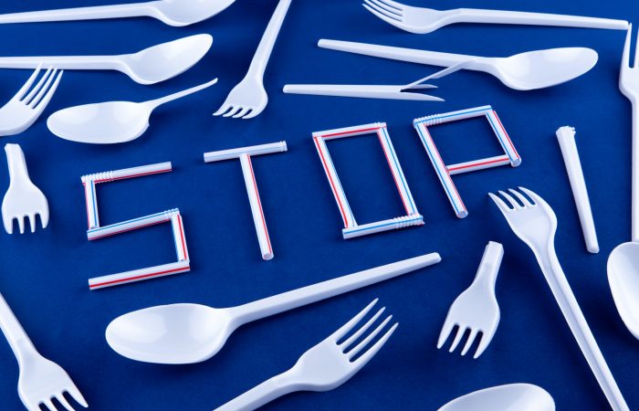 The word stop is written on a blue surface with plastic whistles. Disposable spoons and forks in the background.