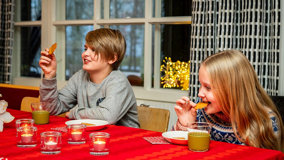Kaksi lasta syö piparia jouluisessa ruokapöydässä.