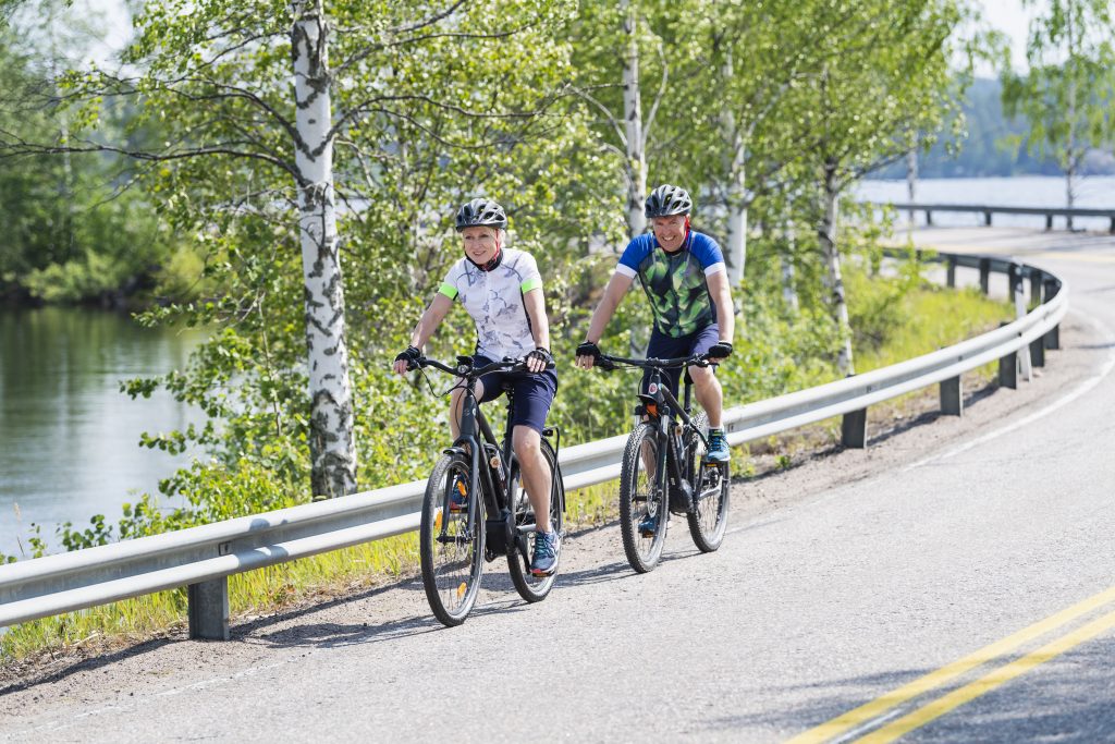 Kaksi pyöräilijää järvimaisemassa.