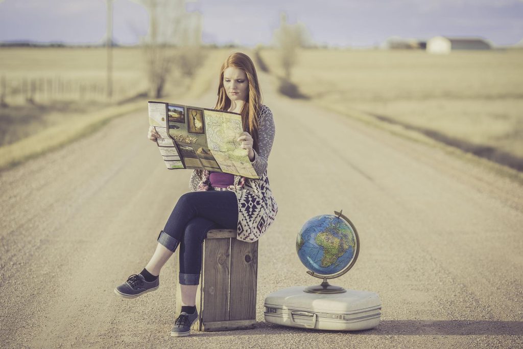 Nainen istuu matkalaukun päällä keskellä tietä karttaa tutkien.