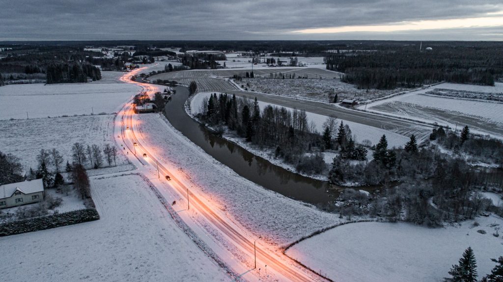 Ilmakuva lumisesta maisemasta. Kuvan poikki menee valaistu autotie.