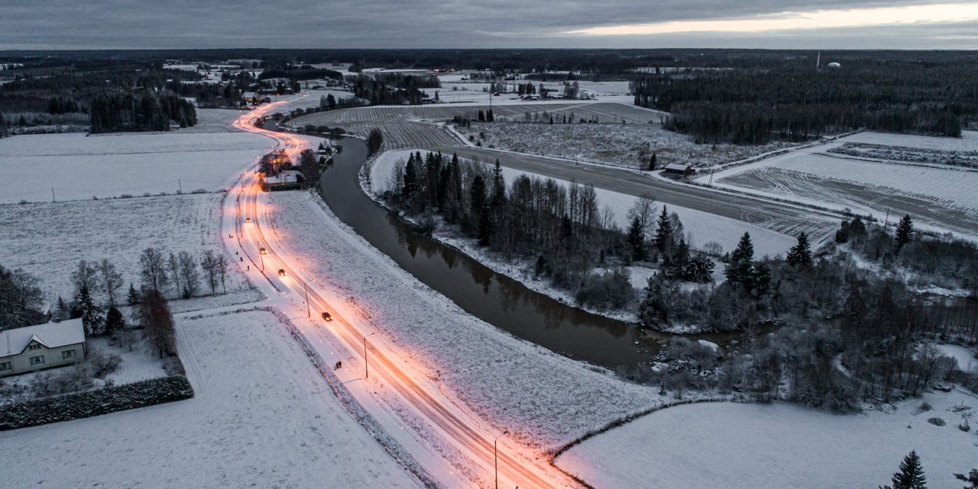 Ilmakuva lumisesta maisemasta. Kuvan poikki menee valaistu autotie.