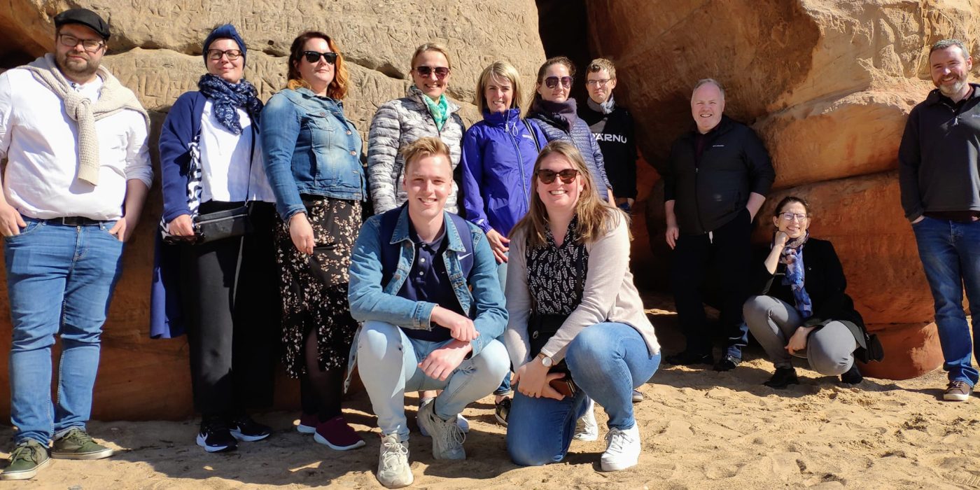 The Latvian consortium members pose for a group photo. A rock in the background.