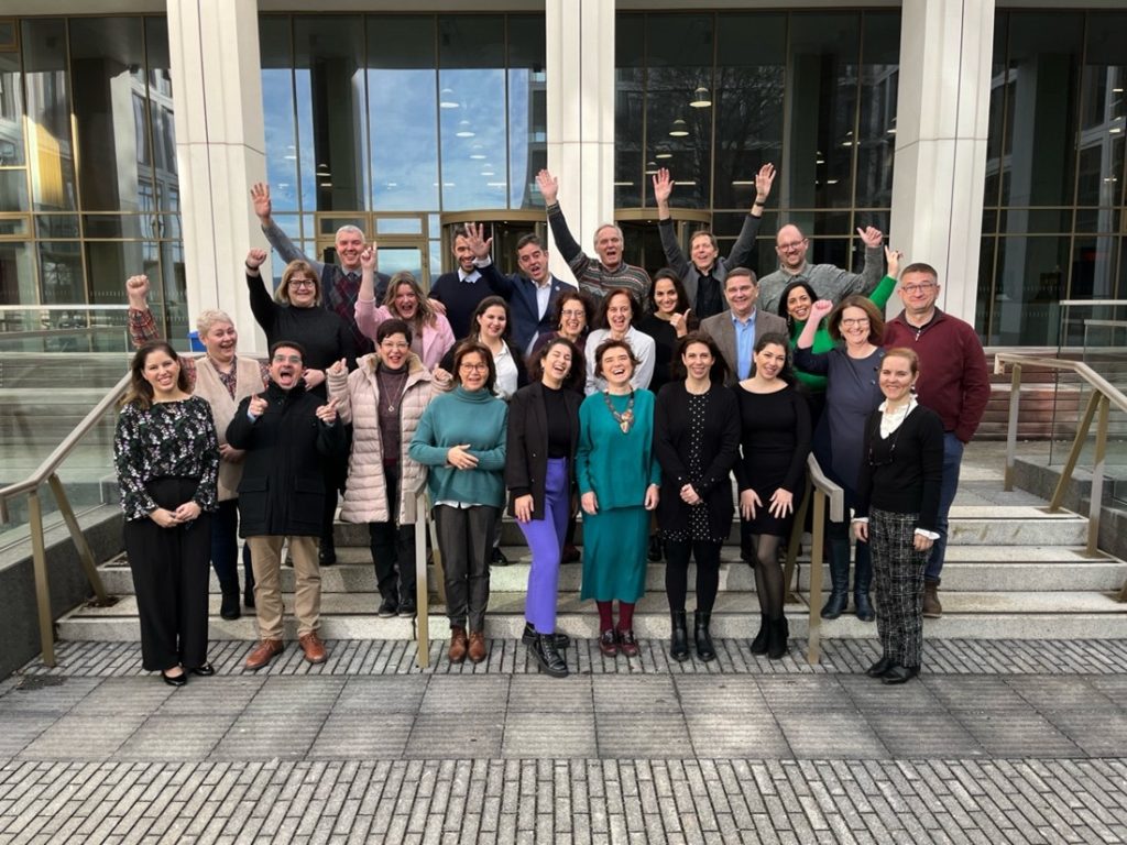 Group of people cheering in a group picture in front of a building.