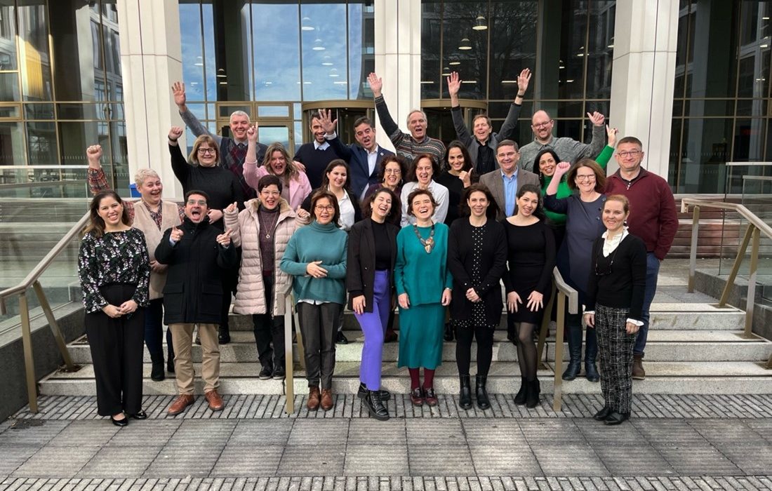 Group of people cheering in a group picture in front of a building.