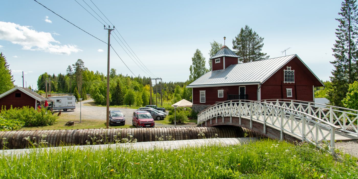 Kaunis vanha rakennus kosken rannassa. Kosken yli menee puinen kaarisilta.
