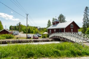 Kaunis vanha rakennus kosken rannassa. Kosken yli menee puinen kaarisilta.