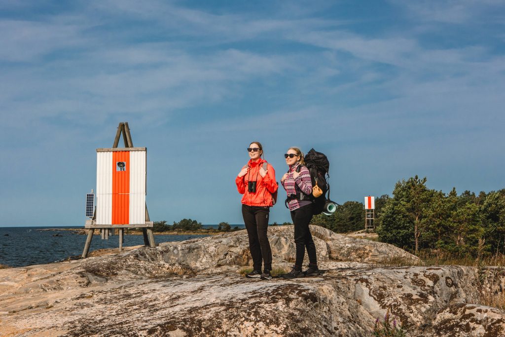 Kaksi naista rinkat selässä kallion päällä meren rannalla.