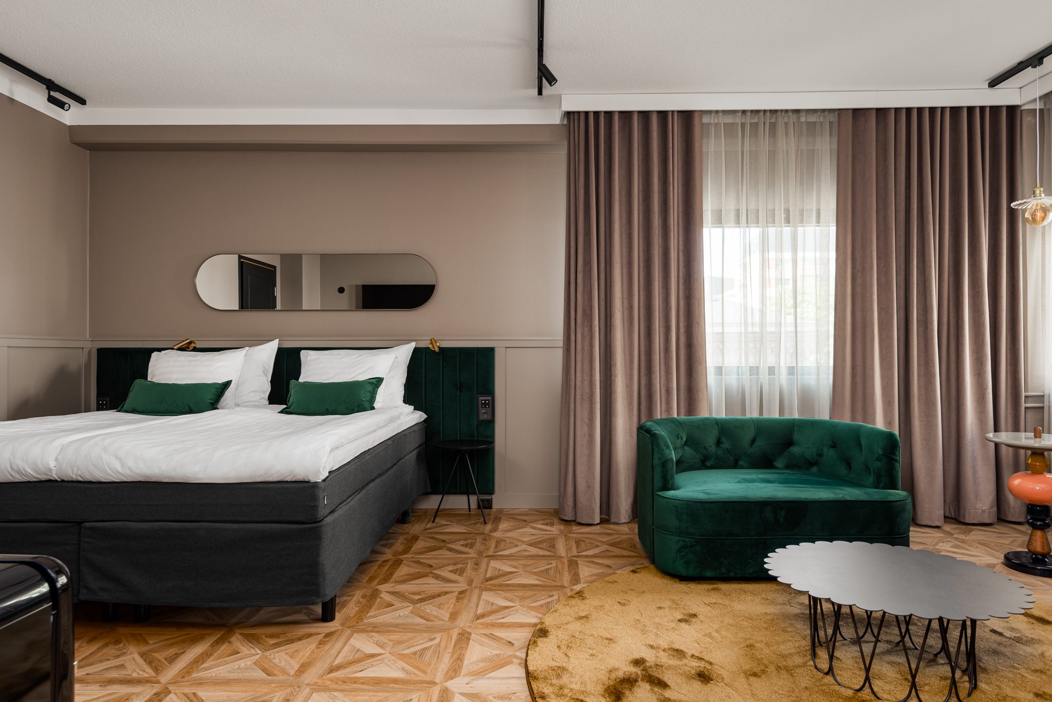 Hotellihuone, jossa sänky, nojatuoli ja ikkunaverhot.