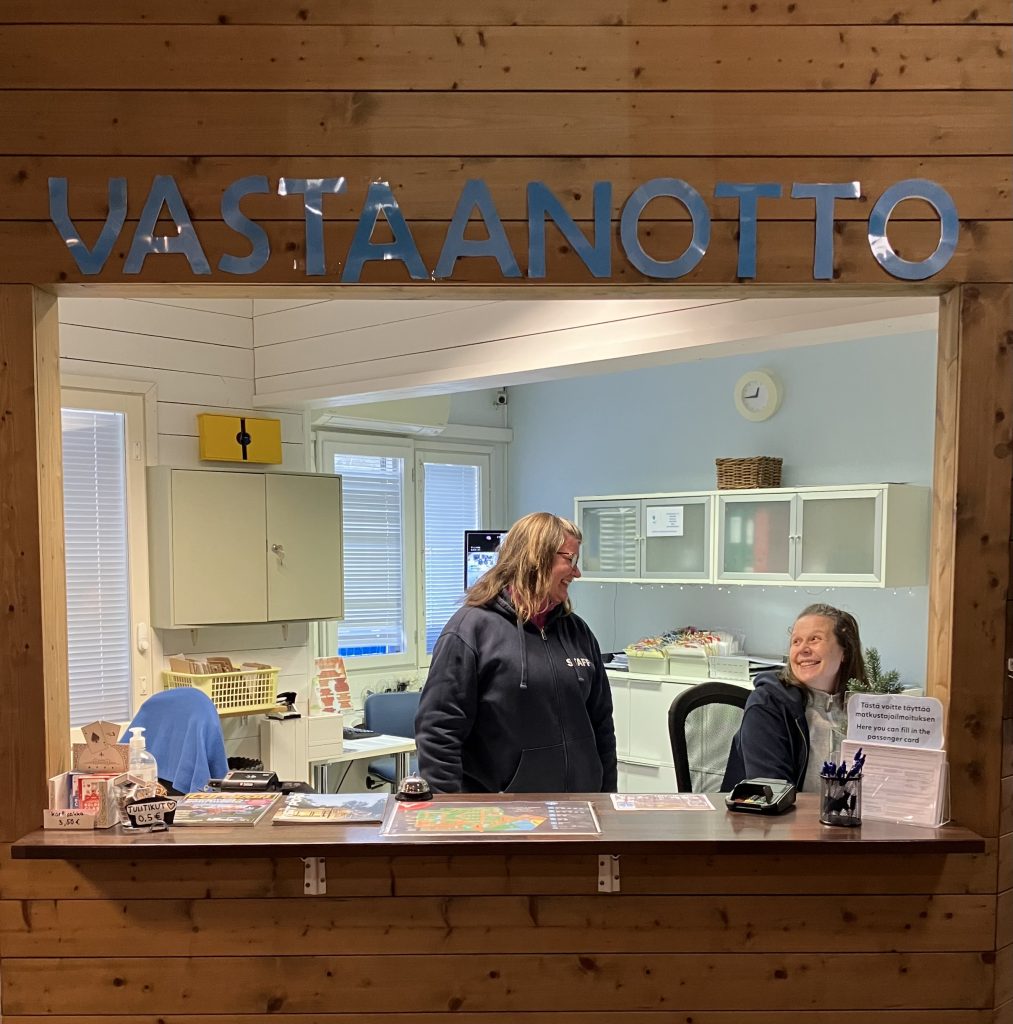 Vastaanoton tiski, kaksi työntekijää ja kyltti “Vastaanotto”.