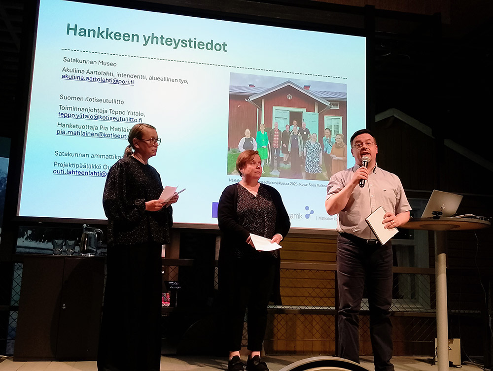 Akuliina Aartolahti, Teppo Ylitalo ja Pia Matilainen puhuvat mikrofoniin esiintymislavalla. Takana Poverpointin diaesitys.