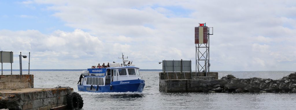 Matkustajavene lähestyy satamalaituria merellä, taustalla rantamerkki ja pilvinen taivas.