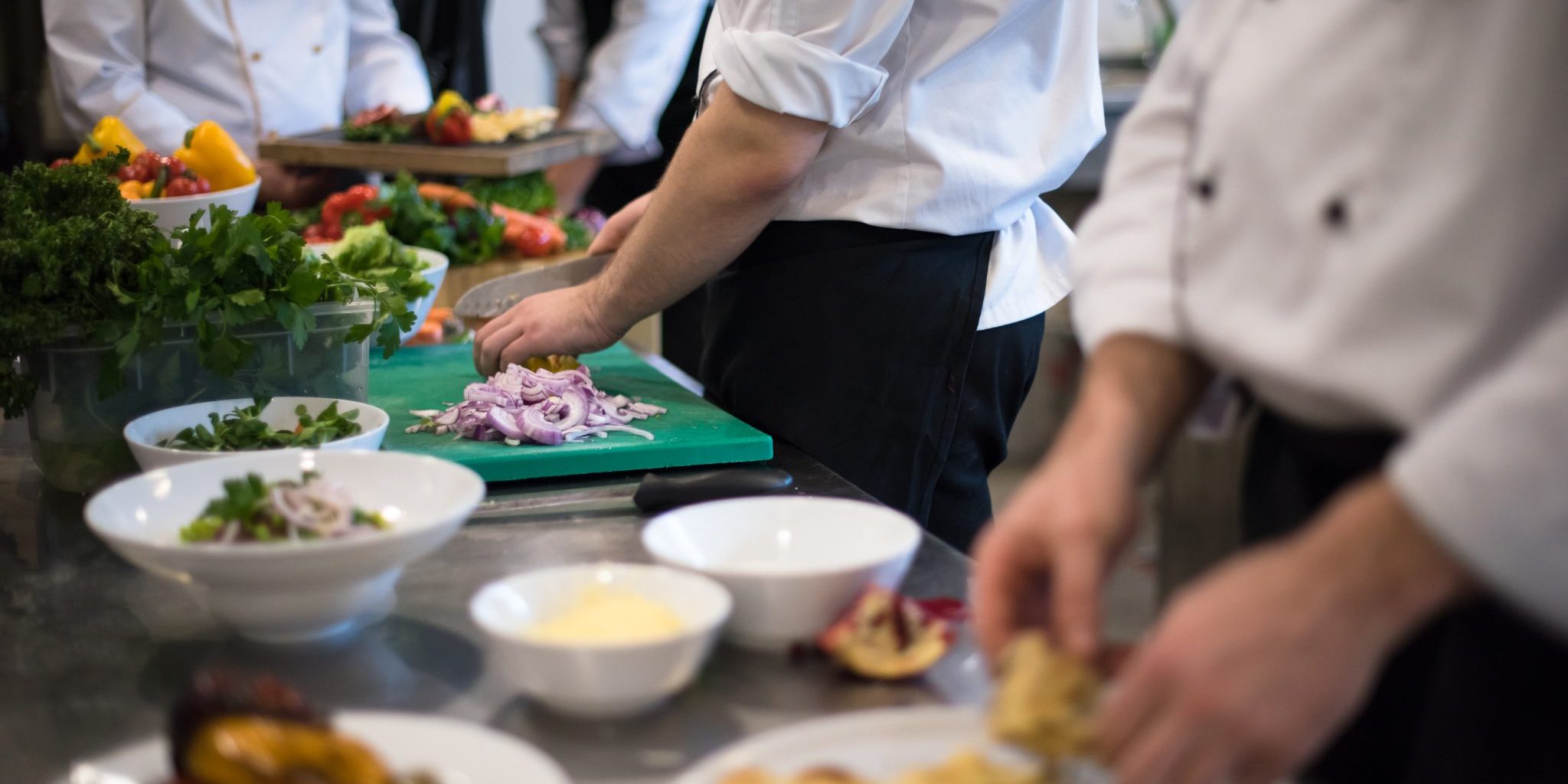 People in chef coats preparing meal at a kitchen.