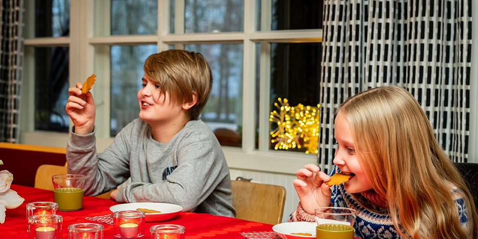 Eino Ja Liina PauliinaPuputti GastroSa 21 Kaksi lasta syö piparia jouluisessa ruokapöydässä.