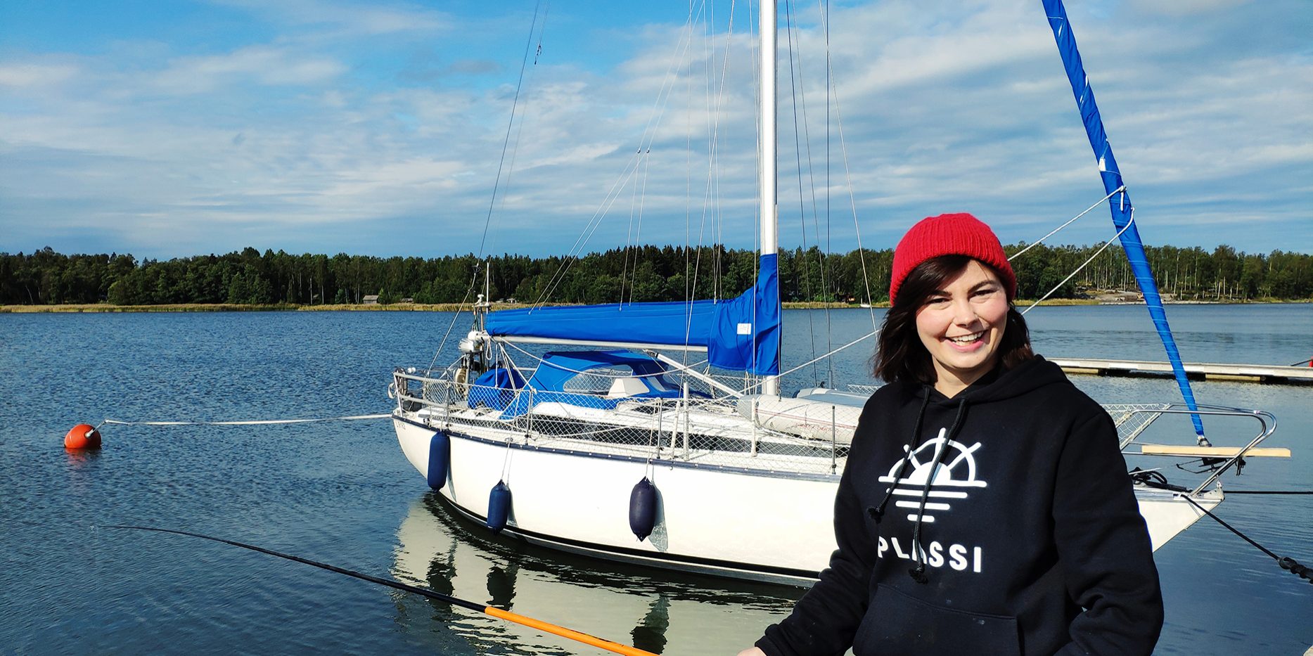 Young woman fishing in the foreground. In the background a sailboat.