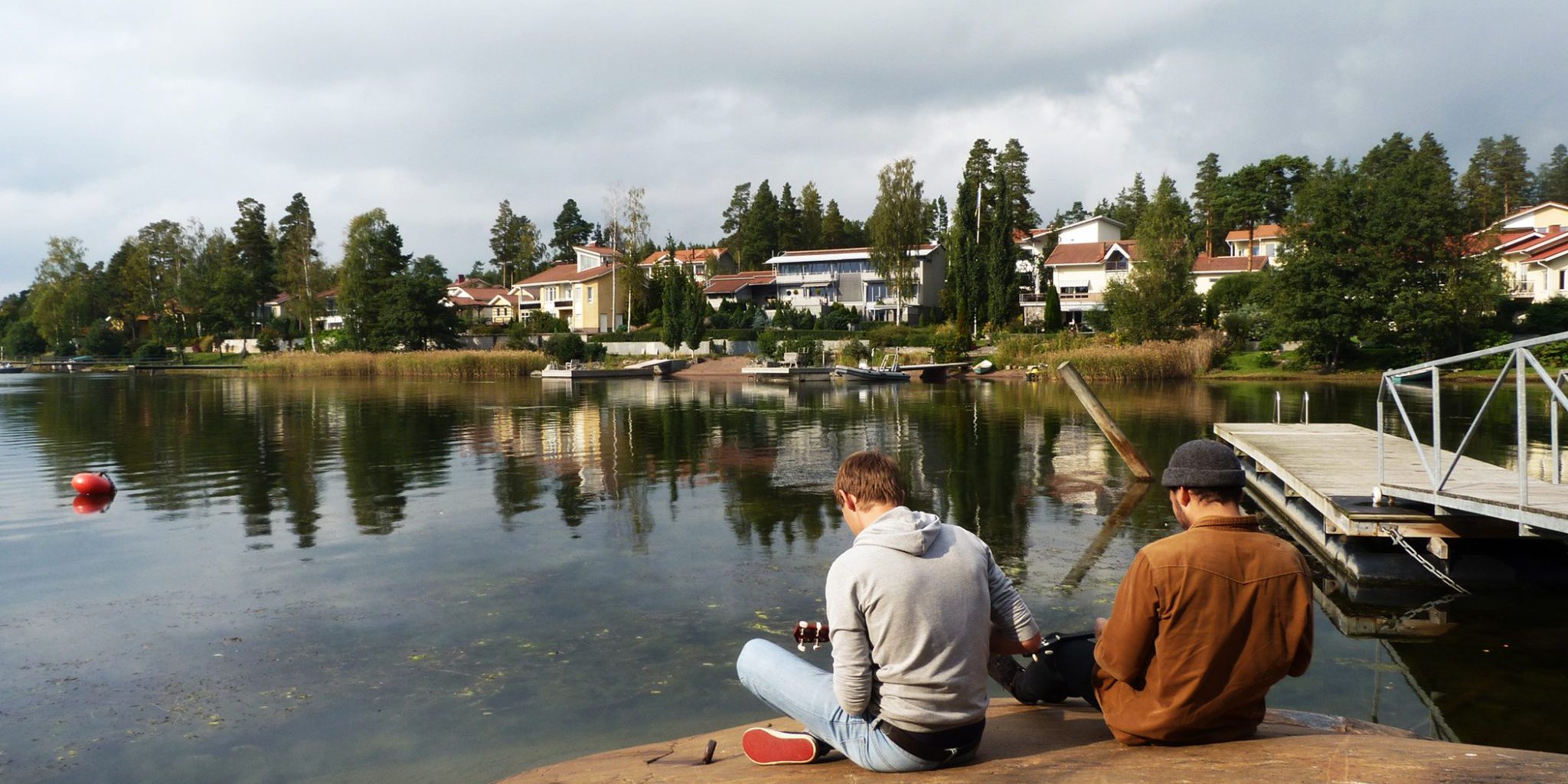 Kaksi miestä istuu selkä päin kameraa kalliolla ja soittaa ukulelejä. Taustalla joki.