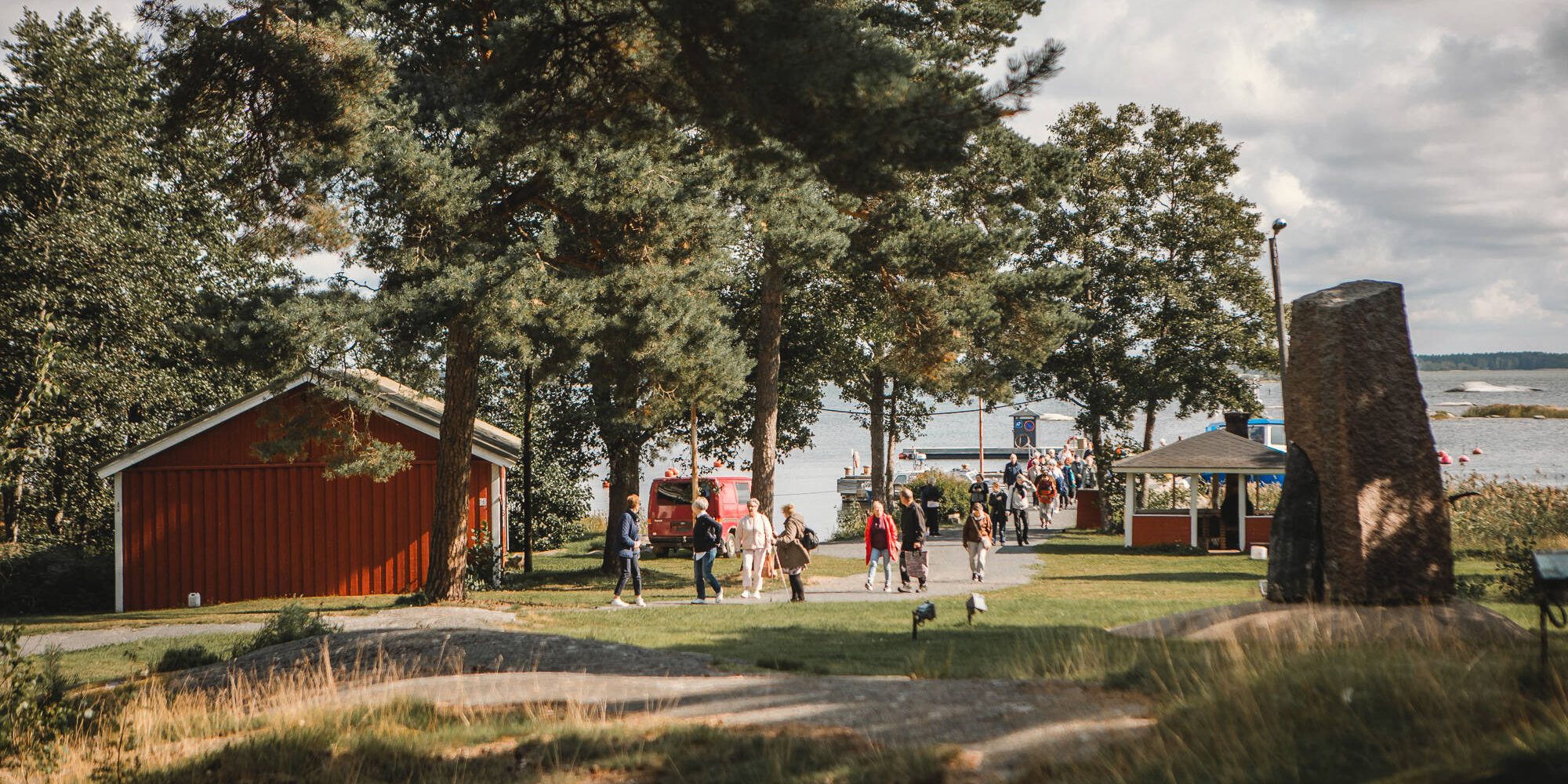 Kuvituskuva. rakennuksia, järvimaisemaa ja ihmisiä.