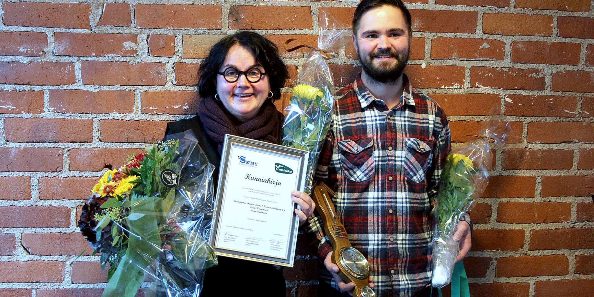 Sirkkaliisa ja Frans Koivuniemi poseeraavat iloisina kukkien ja kunniakirjan kanssa.