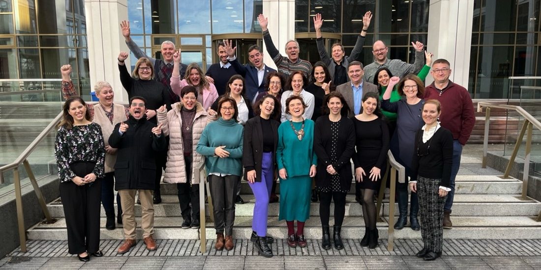 Group of people cheering in a group picture in front of a building.