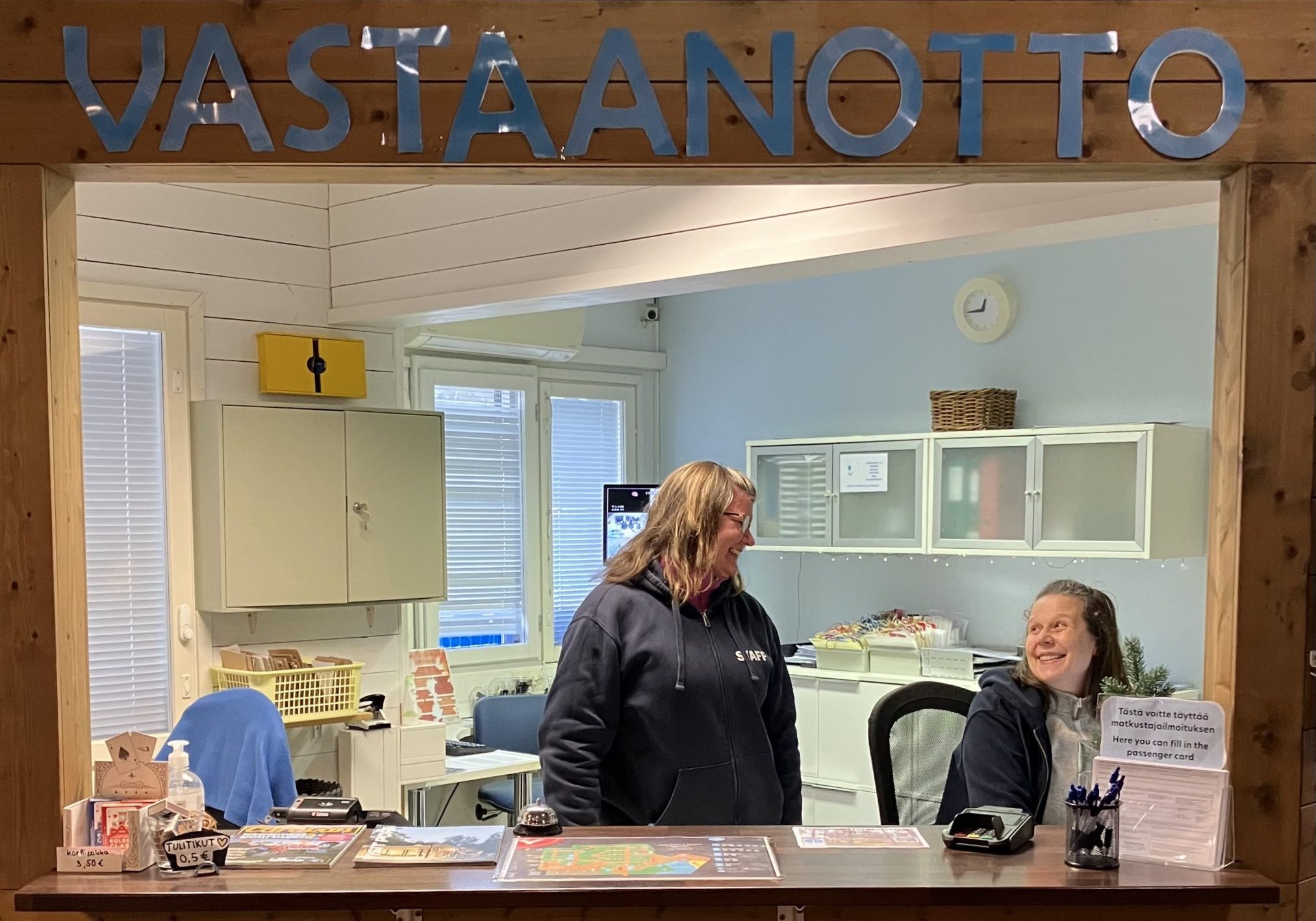 Vastaanoton tiski, kaksi työntekijää ja kyltti “Vastaanotto”.